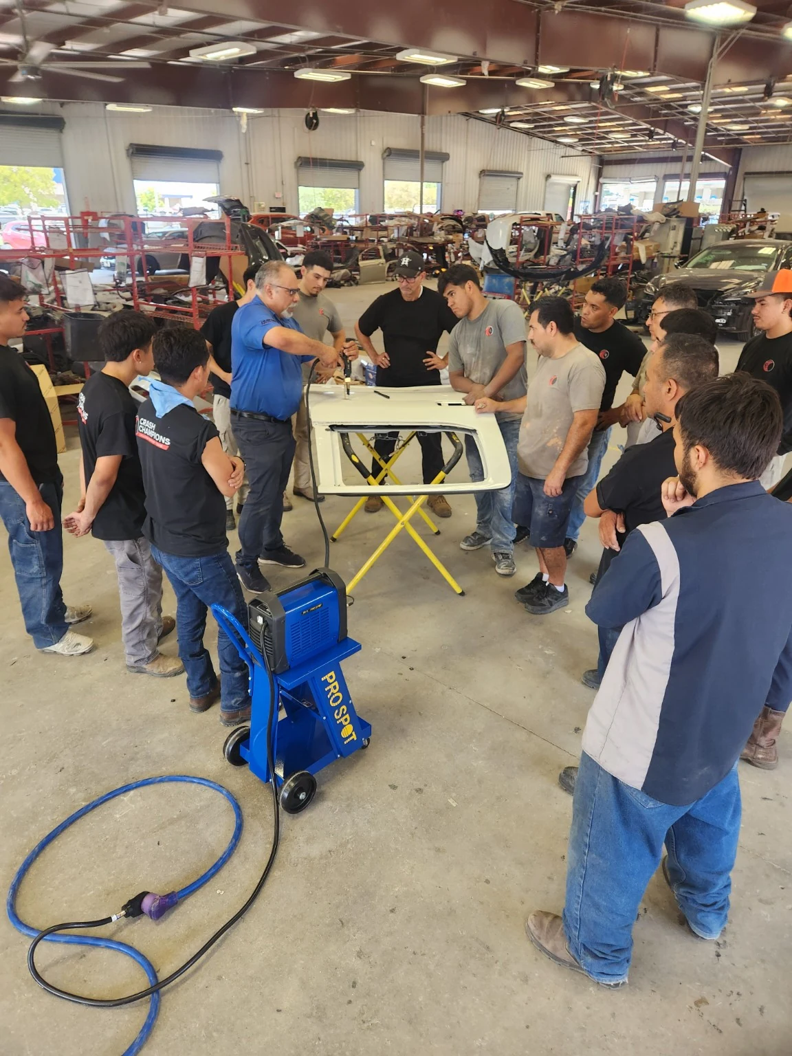 Instructor demonstrating a repair on a vehicle panel to a group of technicians, with Pro Spot equipment in the foreground